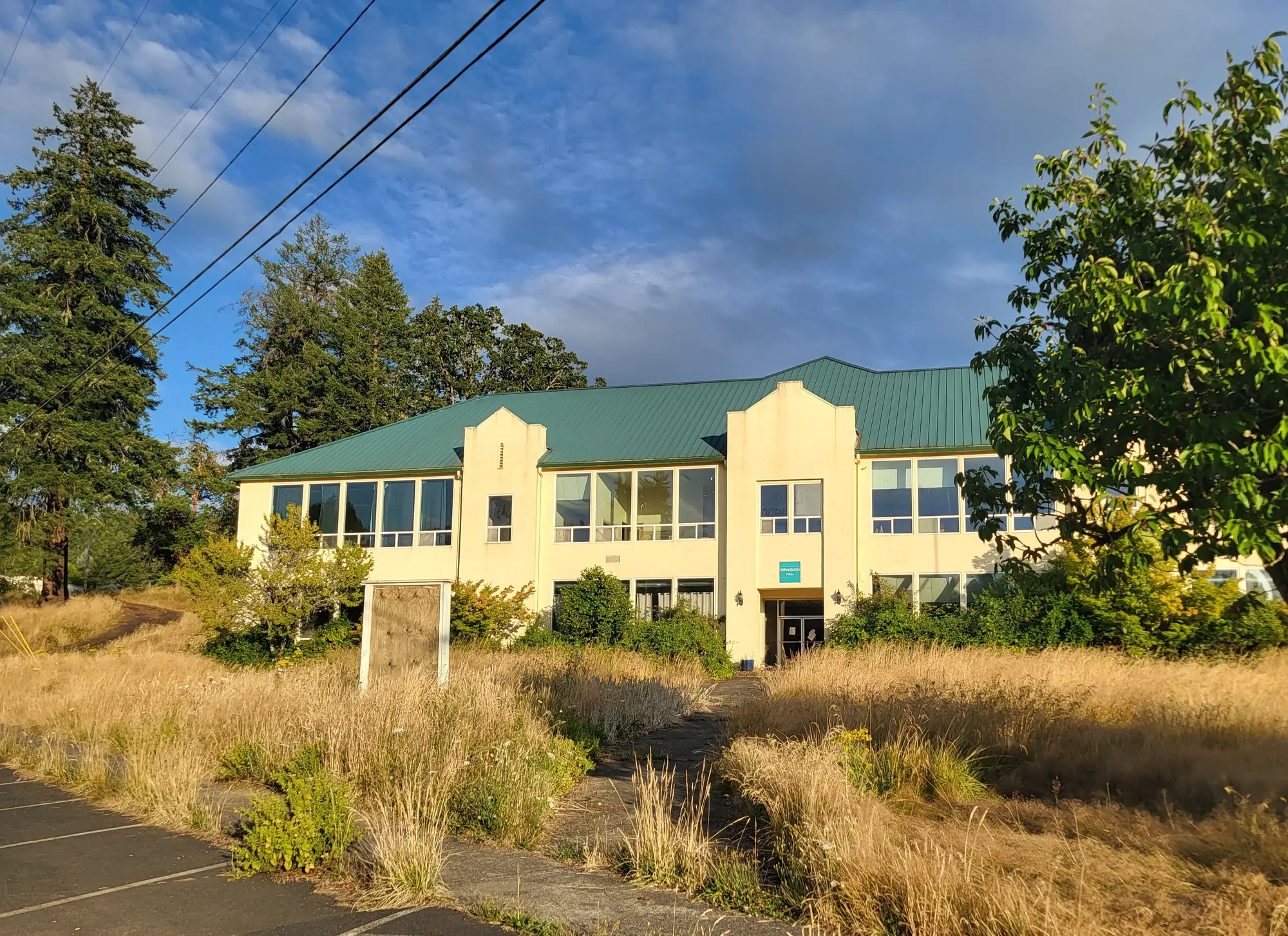 Current front exterior of the main administration building with visible overgrowth and utility lines