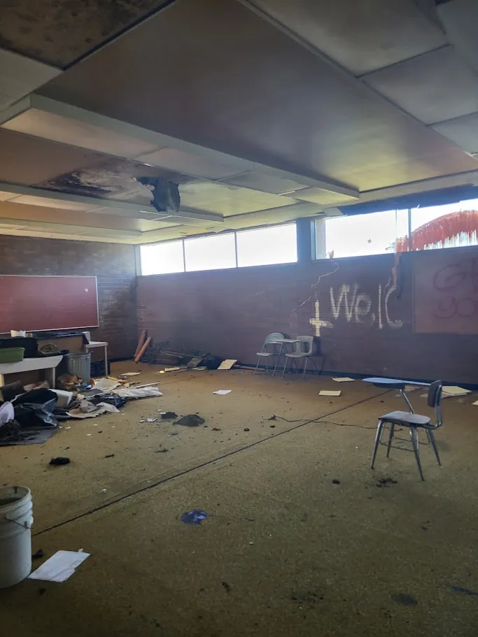 Current classroom interior showing debris, graffiti, and ceiling damage